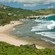 Lush trees through the hills give way to a sandy beach with rolling ocean waves