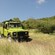 A 6-wheel truck drives down a dirt path amid tall, dry grass