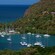 Boats line a bay surrounded by thickly forested hills and houses