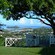 A patio with a wooden fence looks out to the distant water line from the shade of a large tree