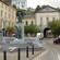 People walk near buildings and a monument with statues