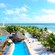 A beach club with a pool, outdoor recliners and a theme of thatched roofs evident in its buildings