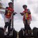 2 women wearing knee pads, safety vests and helmets smile while standing on Segways