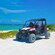 The driver of an all terrain beach buggy gives the thumbs up sign while the passenger admires the views of the ocean