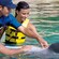 A dolphin floats on its back while a trainer and 2 Guests inspect its belly