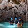 3 pessoas em coletes salva-vidas e capacetes com lanternas exploram uma piscina de água em uma caverna