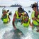 A young family of 5 stand in the shallow waters of the ocean while petting and admiring a stingray
