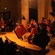A group of performers dressed in tribal clothing dance and play music before an audience
