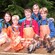 An adult and 4 children smile as they pose next to a wooden table laden with freshly caught fish