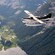 A seaplane flies over a fjord flanked by jagged rocks and pine trees A seaplane flies over a fjord flanked by jagged rocks and pine trees
