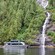 A ferry boat sails in front of a waterfall running off a mountain into the ocean