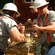 Wood chips fly as 2 lumberjacks saw through a thick log of wood