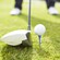 A golf club poised behind a ball on a tee as a golfer prepares to tee off