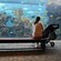 Una mujer sentada en un banco con una carriola cerca de un acuario