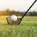 A golf driver rests on the grass behind a ball on a tee