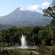 Mount Pelee looms in the background of a lush area with a fountain spraying water