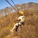 A man wearing a helmet riding a zip line over trees