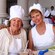 Smiling people wearing chef hats and aprons seated at a table