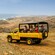 An open air Land Rover Defender filled with passengers is stopped on an undeveloped rocky terrain looking out to the ocean