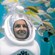 A smiling woman wearing a Sea TREK diving helmet looking at a variety of fish swimming around her