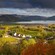 Farms and forests lining the coast of an expansive waterway, with mountains in the distance