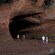 People explore a large cave in a hillside along with its surrounding mudflats