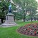 A city park with benches, a gazebo, a flower bed and a bronze statue