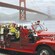 People wave from every seat of a vintage, roofless fire engine with the Golden Gate Bridge in the background