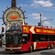 People ride in a red double decker bus with no roof on its second floor in front of a Fishermans Wharf sign
