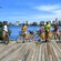 A group of adults and kids with bicycles smile towards the camera on a wooden boardwalk