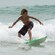 A young boy balances on a surfboard with a wave behind him