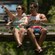 A couple sits in a ski lift chair over a forest