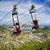 4 people strapped into harnesses on zip lines above a forested island
