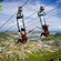 4 people strapped into harnesses on zip lines above a forested island