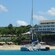 A catamaran docked close to a shoreline of a tropical beach with cabanas, a restaurant and a hotel