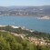 Hillside view of a town on the coast of a bay with and other towns on the far side of the bay.