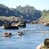 Two inflatable rafts filled with people holding paddles float down rapids with large rocks in the water