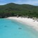 A gorgeous sandy beach is dotted with umbrellas, palm trees and vacationers with lush mountains nearby