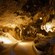An underground cavern features dramatic spotlighting along a dirt path