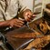 An artisan working with dried tobacco leaves on a workbench equipped with a rolling mold and cutting tools