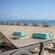 Rolled towels resting on beach lounge chairs, with a row of empty loungers lining the shore near the ocean