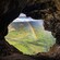 A rainbow over a lush valley and river, framed by the opening of a cave