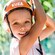 A young girl smiling, wearing a helmet and harness and holding a rope during a zip line course