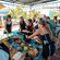 Guests wearing aprons gather around a table filled with fresh vegetables, chips and cooking supplies
