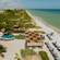 A pool and many lounge chairs, some under a checkered canopy, on a beach fronting the calm waters of the Gulf of Mexico