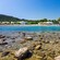 A rocky shoreline in Rhodes, Greece, featuring clear water, lounge chairs and coastal buildings