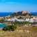 Panoramic view of Lindos featuring coastal buildings, a calm bay and the Acropolis of Lindos