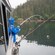 A person fishing from a boat next to fishing rods secured along the boat’s side