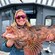 A smiling woman holding a lingcod fish on a fishing boat