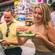 A smiling woman holding a plate of tacos while 2 other Guests enjoy their food at an indoor market